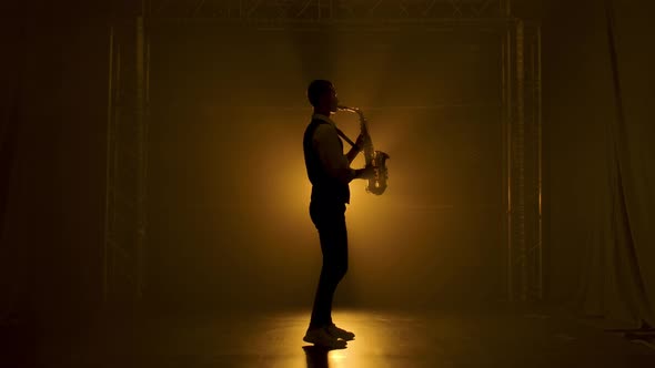 Silhouette a Young Stylish Guy Plays the Golden Shiny Saxophone in the Yellow Spotlights on Stage