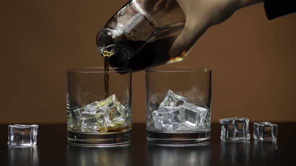 Pouring Whiskey, Cognac Into Glass. Brown Background. Pour of Alcohol Drink