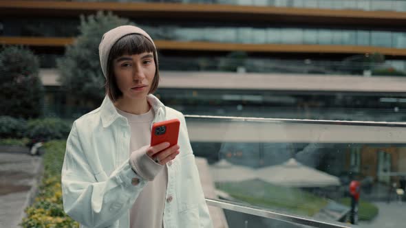 Portrait of Young Woman with Short Dark Hair Using Smartphone and Looking to the Camera Near