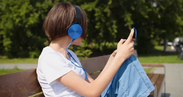 A Teenage Girl Listens to Music in Headphones Through an Online Smartphone Application