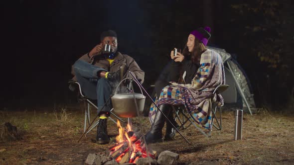 Hikers Toasting with Travel Mugs By Bonfire at Dusk