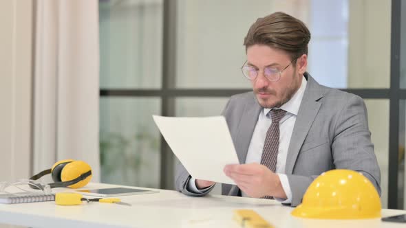 Middle Aged Engineer Reading Reports while Sitting in Office