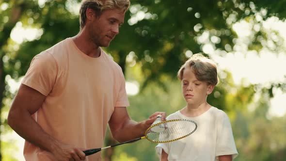 A happy father is teaching his son playing badminton