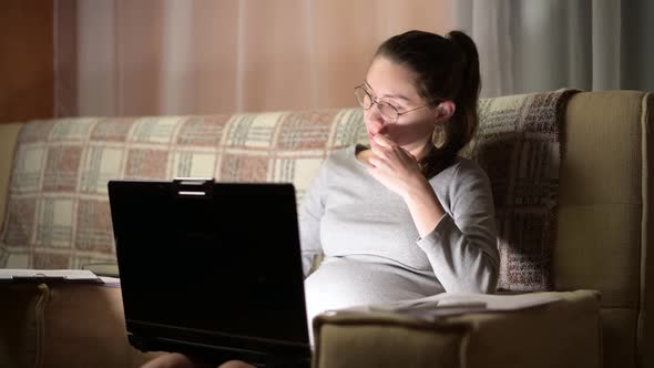 Young pregnant woman working on a laptop at home on the couch. Remote work