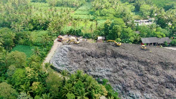 Excavators work on trash pile in tropical forest on Java, Indonesia