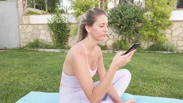 Tranquil woman using smartphone on mat in courtyard