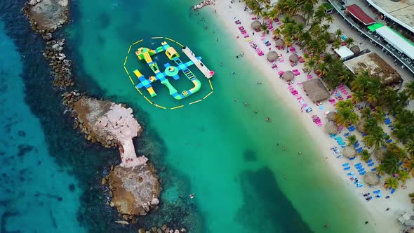 Aerial view dolly in Mambo Beach, inflatables in the water, Curacao, Dutch Caribbean island. Palm tr