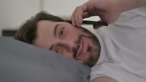 Portrait of Young Man Talking on Call on Smartphone in Bed