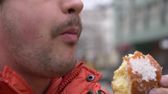 man eating traditional polish donut on city street