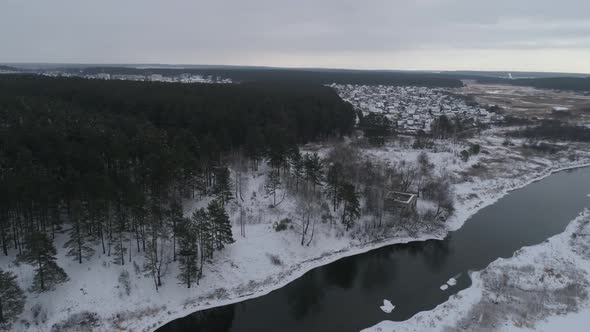 Aerial view of winter river near the forest. In the far village. Mainly cloudy 05