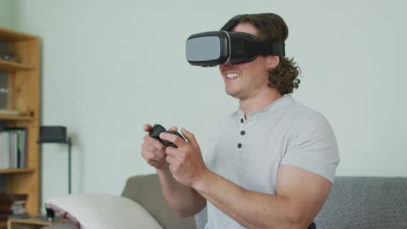 Happy caucasian man wearing vr headset and holding game pad in living room