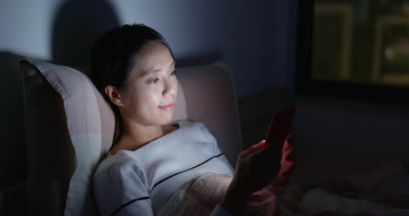 Woman watch on cellphone on bed at night