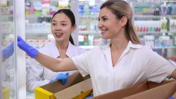 Portrait of Positive Asian New Employee Talking with Professional Caucasian Pharmacist in Drugstore