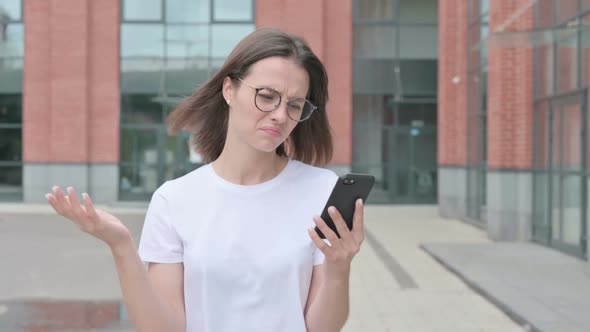 Young Woman Reacting to Loss on Smartphone while Walking on Street