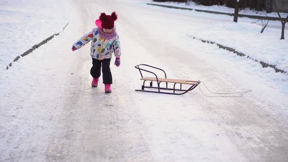 Happy Little Funny White Preschool Girl In Colorful Jacket With Sled Fell On Snow In Winter