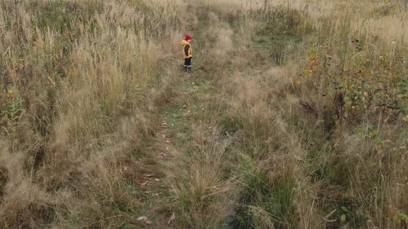 Boy Child in a Yellow Vest and Red Hat Runs