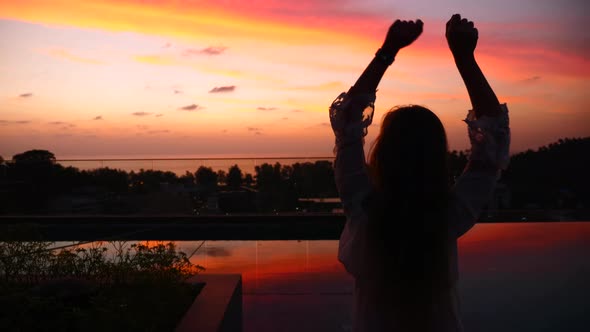 Silhouette of Happy Woman Dancing with Amazing Sunset View on Rooftop Hotel