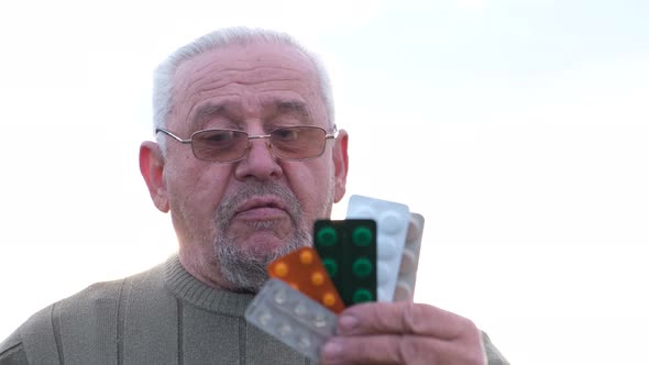 Sick Old Mature Grayhaired Man Grandfather Holding a Pack of Pills in His Hands