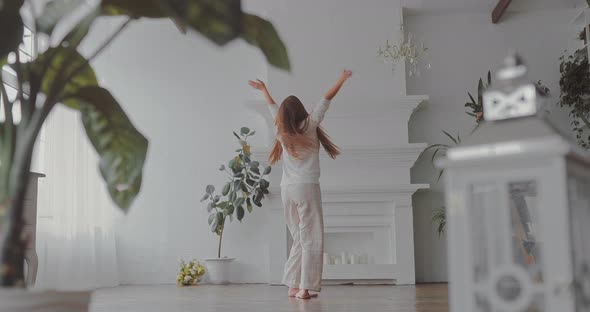 Young Happy Woman is Spinning Around Herself in a Bright Room Having Fun in Her Pajamas