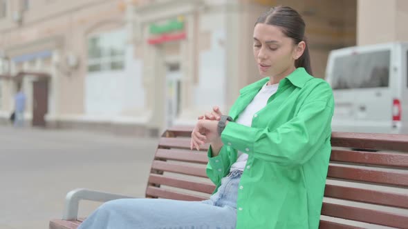 Hispanic Woman Checking Time While Waiting on Bench Outdoor
