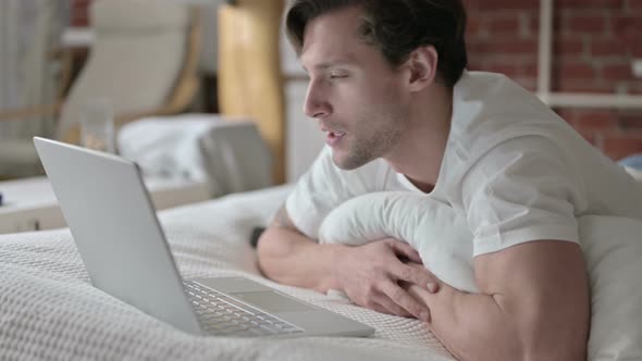 Ambitious Young Man Doing Video Chat on Laptop in Bed