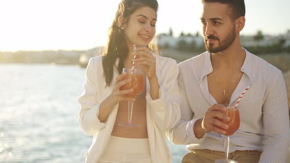 Content Ethnic Couple Drinking Cocktails and Talking on Embankment