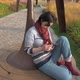 Caucasian Woman Sitting on a Round Park Bench with a Phone in Her Hands - VideoHive Item for Sale