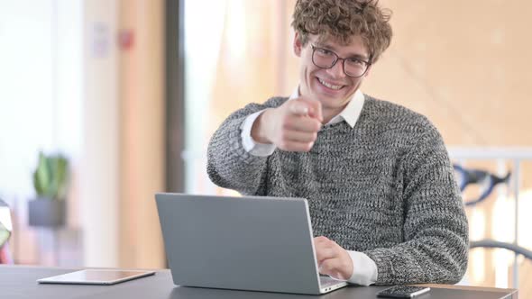 Young Man with Laptop Pointing at Camera