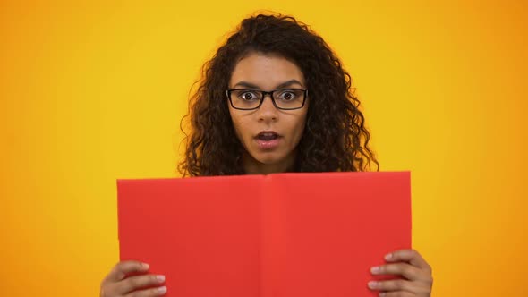 Smart Biracial Female Millennial Shocked With Scientific Facts, Holding Red Book