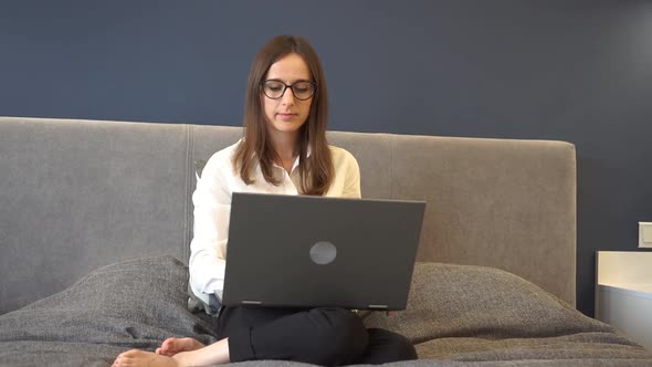 Portrait of Attractive Freelancer Girl in Glasses with a Laptop on the Bed in Hotel