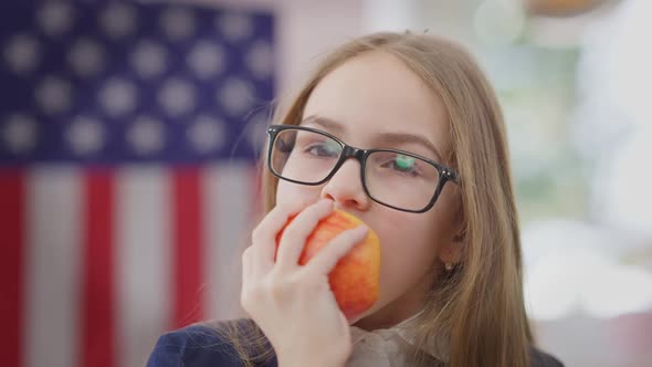 Headshot Portrait of Positive Pretty Schoolgirl Eating Vitamin Apple Looking at Camera Smiling