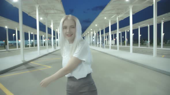 Young Beautiful Woman with White Hair in a Short Skirt is Dancing on the Background of an Empty Car