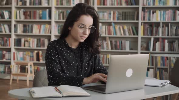 Smiling Young Woman Student in Library  Looking at Laptop Screen Watching Educational Video Online