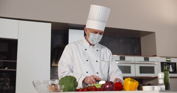 Senior Male Chef Wearing Safety Mask Cooking in Modern Kitchen