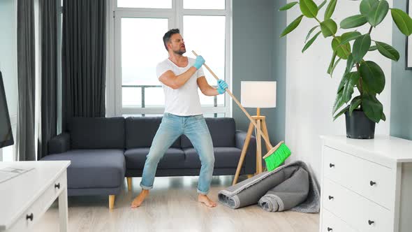 Man Cleaning the House and Having Fun Dancing and Singing with a Broom