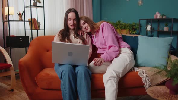 Young Adult Women Couple Looking at Laptop Notebook Screen Making Online Shopping Purchase at Home