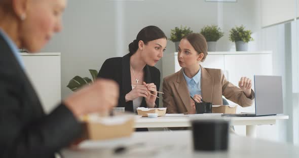 Business People Sitting at Table in Front of Laptop and Having Lunch Together in Office