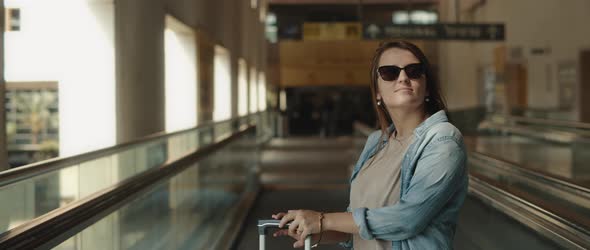 Woman on a Moving Walkway with Her Suitcase, Looking Around