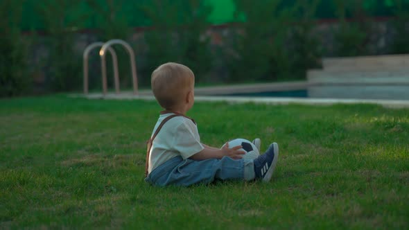 Toddler Sits on Soft Grass Throwing Soccer Ball to Mother