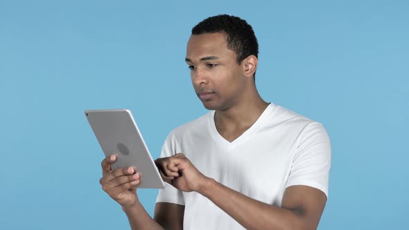 Young African Man Excited for Success While Using Tablet Blue Background