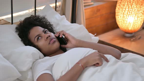 Young African Woman Talking on Smartphone Laying in Bed 