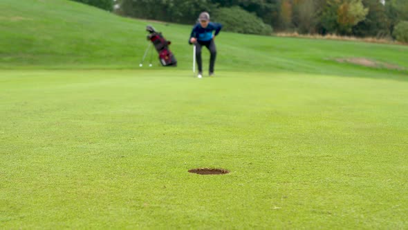 Blurred out golfer lining up for a medium length putt with focus on the hole.