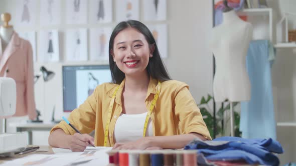 Female Designer With Sewing Machine Smiling To The Camera While Designing Clothes In The Studio