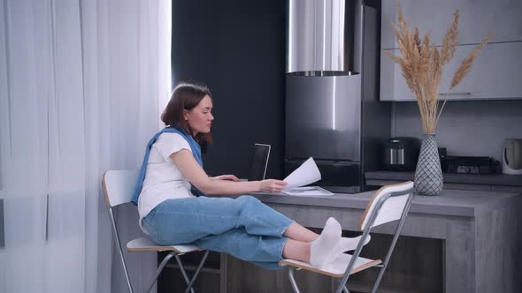 Young Woman Working Remotly From Her Dining Table. Home Kitchen in the Background