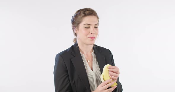 Woman peeling and eating a banana on a white studio background