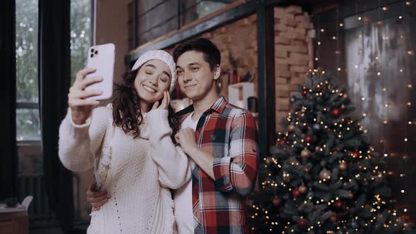 Young Couple Dressed in Christmas Clothes, Having Fun and Taking Pictures with Their Phone Near the