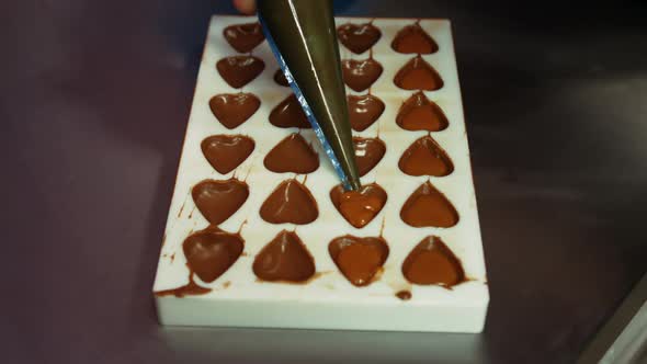 Worker filling chocolate moulds with melted chocolate