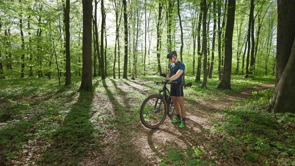 A Cyclist is Standing in the Middle of the Forest and Looking at the Training Data on His Smartphone