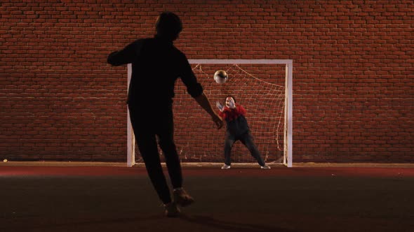 Two Young Friends Playing Football on the Outdoor Playground at Night - Protecting the Football