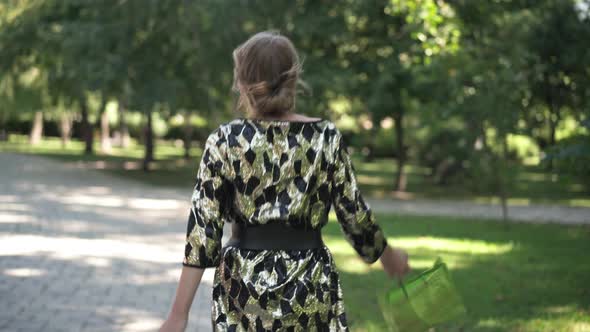 Young Slim Drunk Woman in Party Dress Walking on Sunny Morning in City Park Spinning Singing